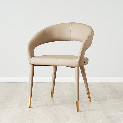 Modern Dining Chair with a curved backrest design, angular armrests and open back, wrapped in sand beige vegan leather, supported by four legs with golden tips.